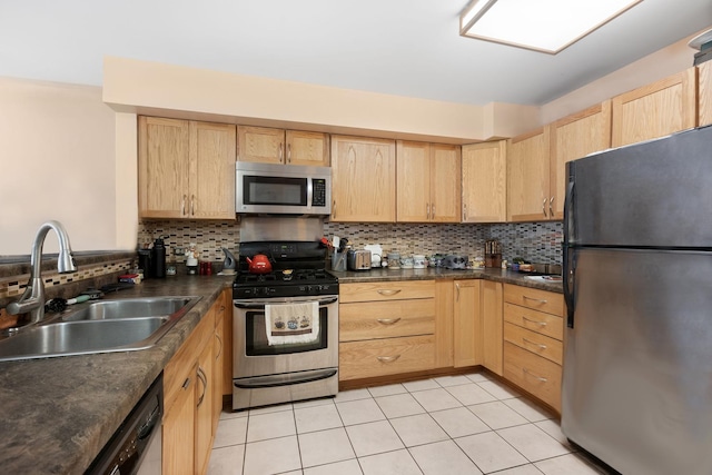 kitchen featuring tasteful backsplash, dark countertops, stainless steel appliances, light brown cabinets, and a sink