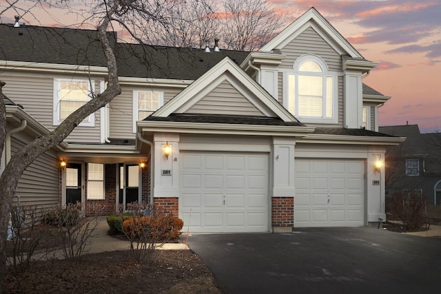 traditional-style house featuring roof with shingles, aphalt driveway, and brick siding