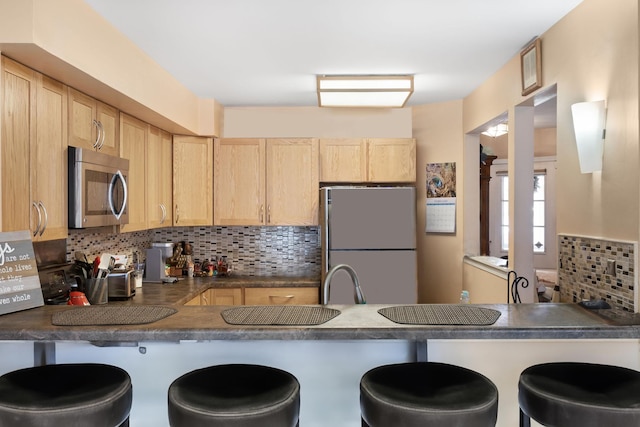 kitchen with freestanding refrigerator, stainless steel microwave, a peninsula, and light brown cabinets