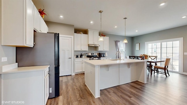 kitchen with white cabinets, under cabinet range hood, range, and a sink