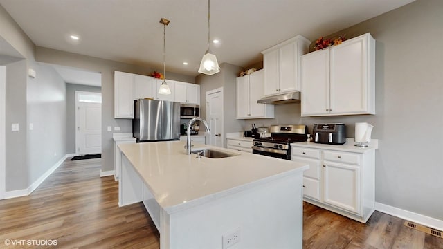 kitchen featuring a center island with sink, stainless steel appliances, light wood-style floors, a sink, and under cabinet range hood