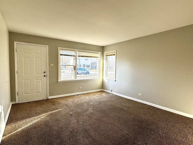 spare room with dark colored carpet, visible vents, and baseboards