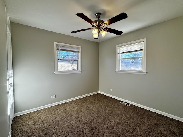 empty room featuring a healthy amount of sunlight, visible vents, baseboards, and dark colored carpet