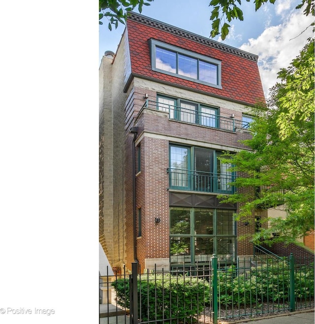 view of front of home with mansard roof, a balcony, a fenced front yard, a high end roof, and brick siding