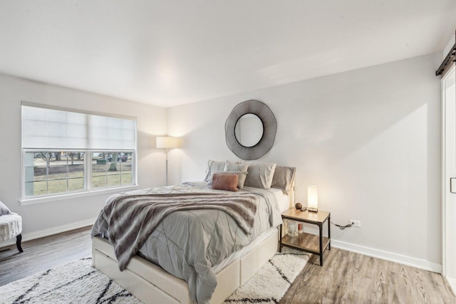 bedroom with a barn door, light wood-style flooring, and baseboards