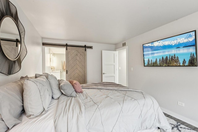 bedroom with a barn door, visible vents, baseboards, connected bathroom, and wood finished floors