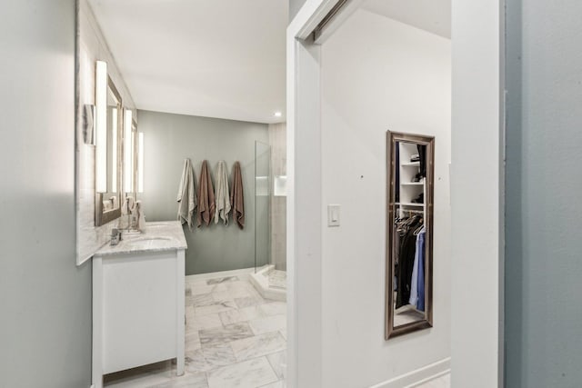 full bathroom featuring a walk in closet, marble finish floor, a stall shower, vanity, and baseboards