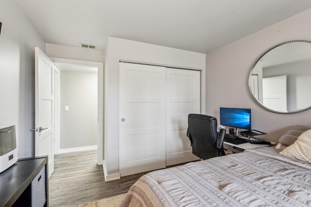 bedroom with baseboards, a closet, visible vents, and wood finished floors