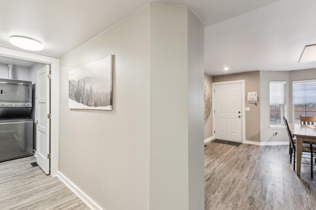 hallway featuring stacked washing maching and dryer, wood finished floors, and baseboards