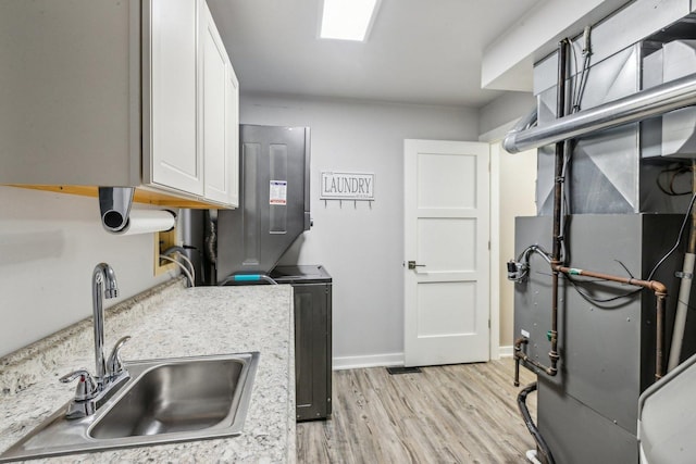 kitchen featuring heating unit, light countertops, light wood-type flooring, white cabinetry, and a sink