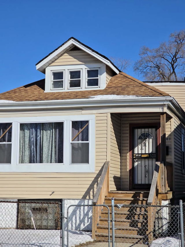 view of front facade with roof with shingles, a fenced front yard, and a gate