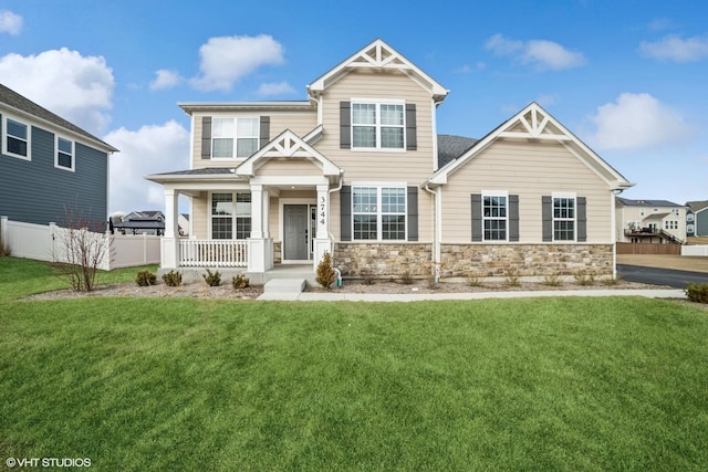 craftsman-style house with covered porch, stone siding, a front lawn, and fence