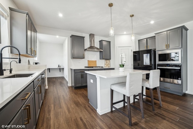 kitchen with stainless steel appliances, dark wood-type flooring, a sink, a kitchen breakfast bar, and wall chimney range hood