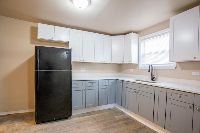 kitchen featuring a sink, light countertops, gray cabinets, freestanding refrigerator, and light wood finished floors