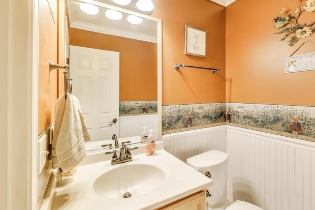 half bath with toilet, a wainscoted wall, crown molding, and vanity