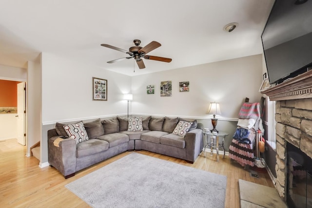 living area with baseboards, a ceiling fan, wood finished floors, and a stone fireplace