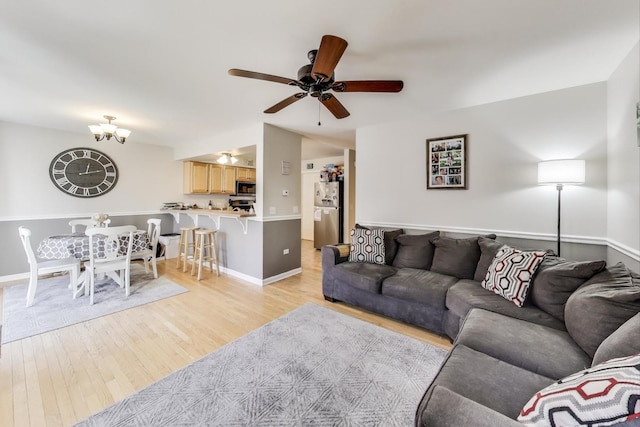 living area featuring ceiling fan with notable chandelier, baseboards, and light wood-style floors