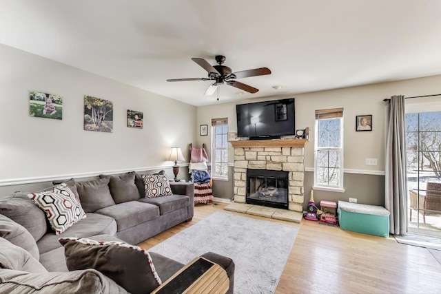 living area featuring a wealth of natural light, ceiling fan, a stone fireplace, and wood finished floors