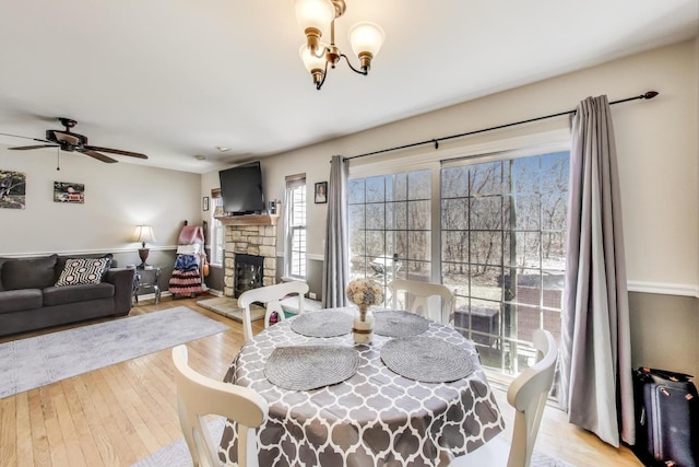 dining room featuring ceiling fan, wood finished floors, and a stone fireplace