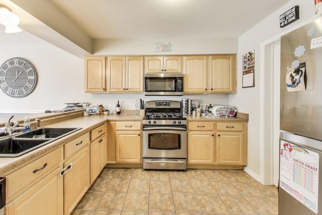 kitchen with appliances with stainless steel finishes, light tile patterned floors, a sink, and light brown cabinetry