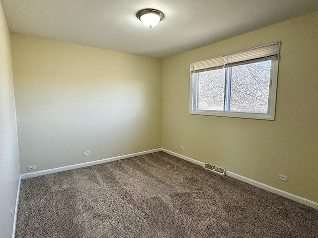 spare room featuring dark colored carpet, visible vents, and baseboards