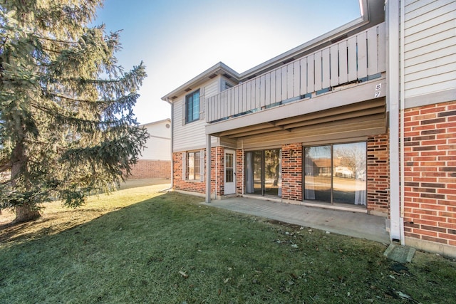 back of property with a yard, brick siding, a patio, and a balcony