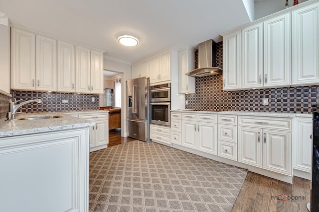 kitchen with backsplash, appliances with stainless steel finishes, ornamental molding, a sink, and wall chimney exhaust hood