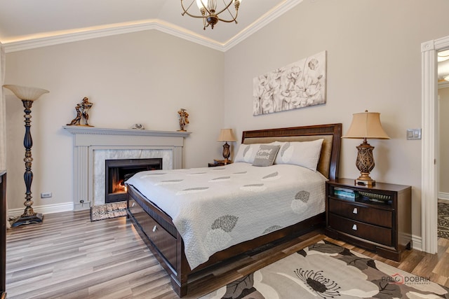 bedroom with crown molding, a high end fireplace, vaulted ceiling, wood finished floors, and baseboards