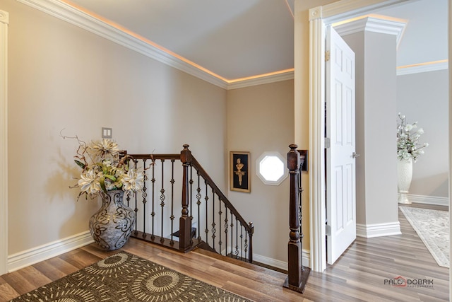 staircase with ornamental molding, wood finished floors, and baseboards