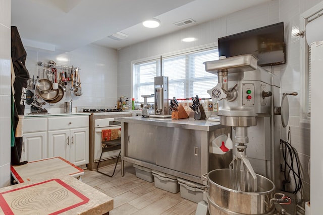 kitchen with high end stove, visible vents, white cabinets, light countertops, and light wood finished floors