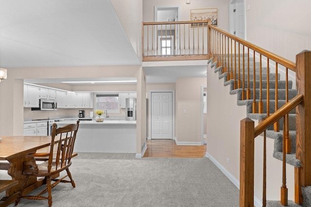 dining room featuring stairs, baseboards, a towering ceiling, and light colored carpet