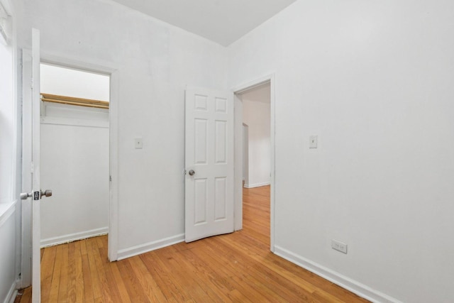 unfurnished bedroom featuring a closet, a spacious closet, baseboards, and wood finished floors