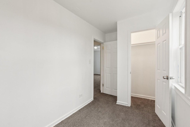 unfurnished bedroom with dark colored carpet, a closet, a walk in closet, and baseboards