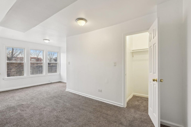 interior space with dark colored carpet, a spacious closet, a closet, and baseboards