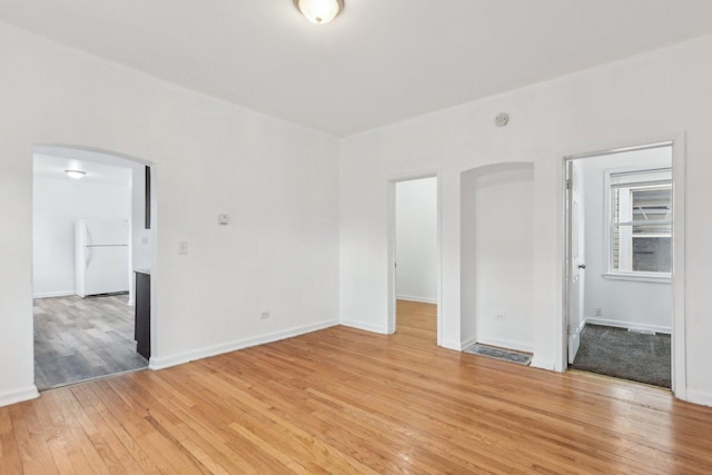 unfurnished room featuring arched walkways, light wood finished floors, visible vents, and baseboards