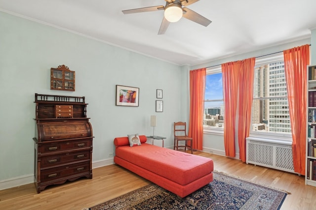 sitting room with radiator heating unit, a ceiling fan, ornamental molding, wood finished floors, and baseboards