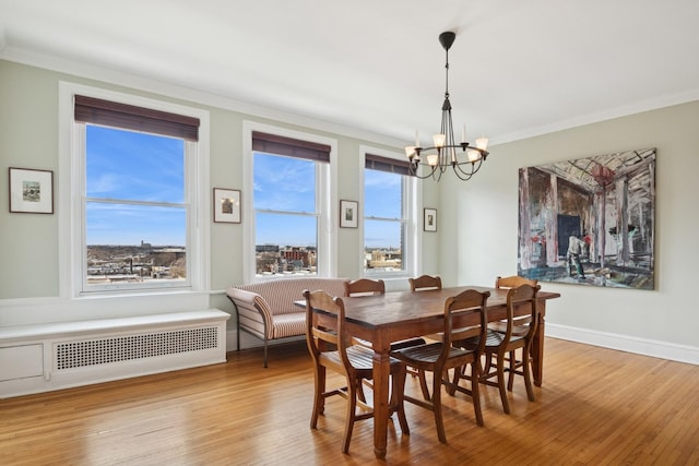 dining space with baseboards, radiator, wood finished floors, an inviting chandelier, and crown molding