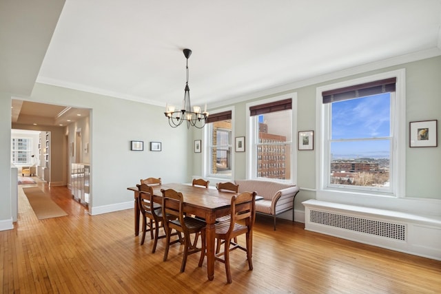 dining space with crown molding, light wood finished floors, radiator, a chandelier, and baseboards