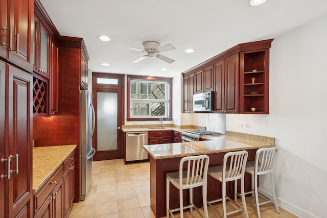 kitchen featuring a peninsula, light stone countertops, stainless steel appliances, dark brown cabinets, and a sink