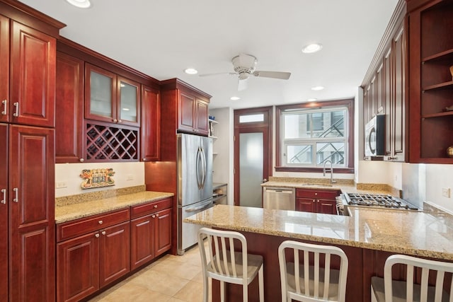 kitchen featuring reddish brown cabinets, appliances with stainless steel finishes, light stone countertops, open shelves, and a sink