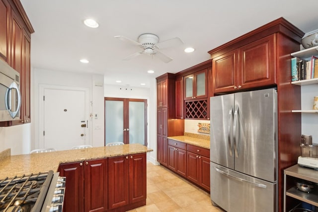 kitchen featuring reddish brown cabinets, a ceiling fan, appliances with stainless steel finishes, light stone counters, and recessed lighting