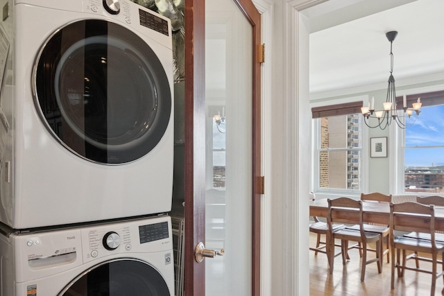 laundry room with laundry area, stacked washing maching and dryer, wood finished floors, and a notable chandelier