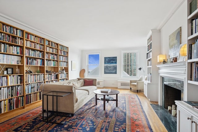 living area with wood finished floors, crown molding, wall of books, and a premium fireplace