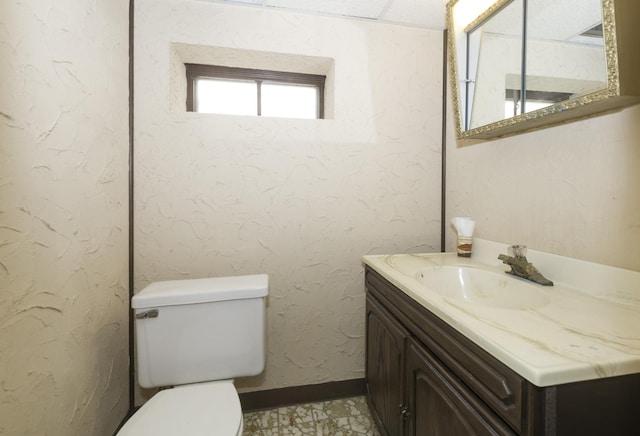 half bath featuring toilet, a textured wall, baseboards, and vanity