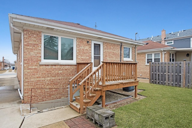 back of house with brick siding, a lawn, and fence