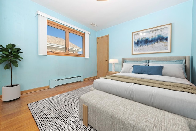 bedroom with a baseboard radiator, baseboards, and wood finished floors