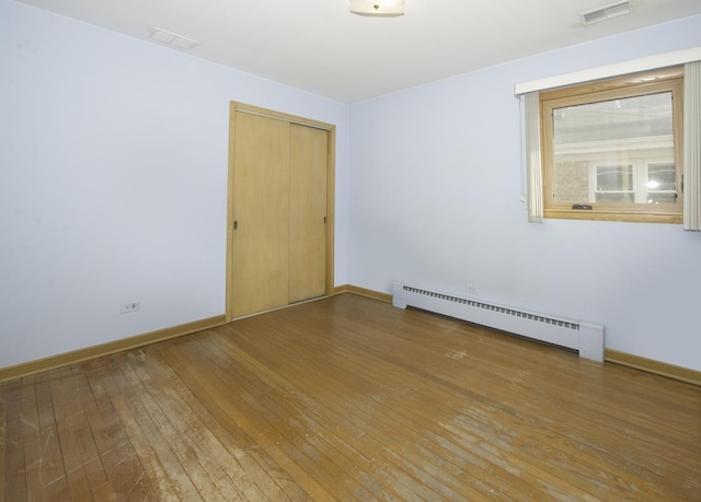 unfurnished room featuring a baseboard radiator, visible vents, wood-type flooring, and baseboards