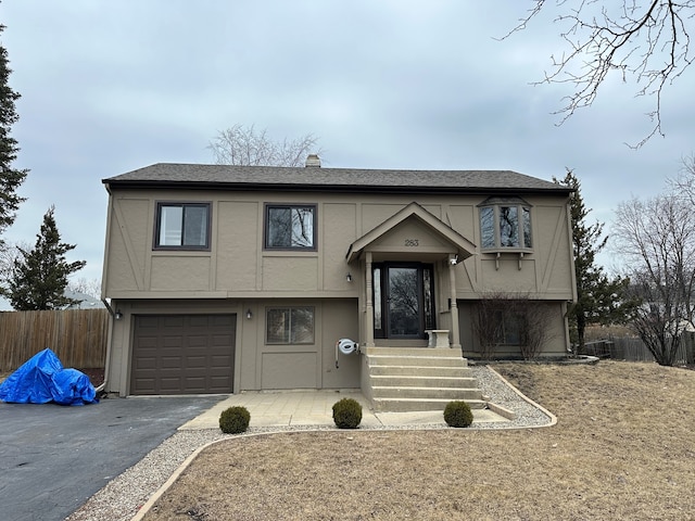 bi-level home with a garage, a shingled roof, fence, driveway, and stucco siding