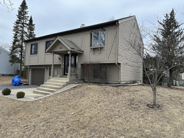 bi-level home with a garage, driveway, a chimney, and stucco siding