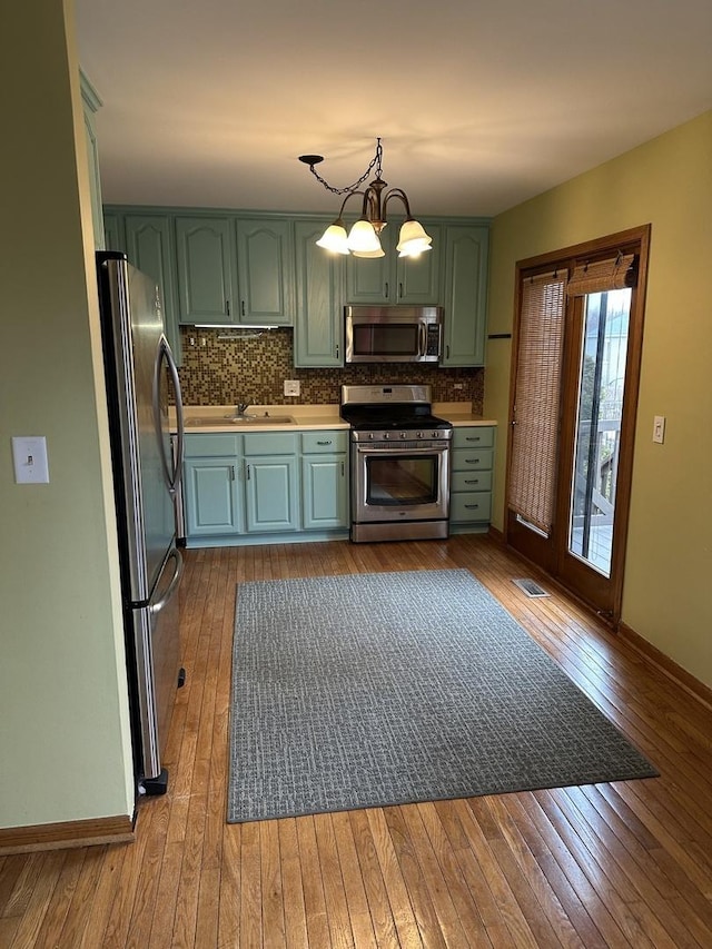 kitchen with green cabinets, appliances with stainless steel finishes, backsplash, dark wood finished floors, and an inviting chandelier